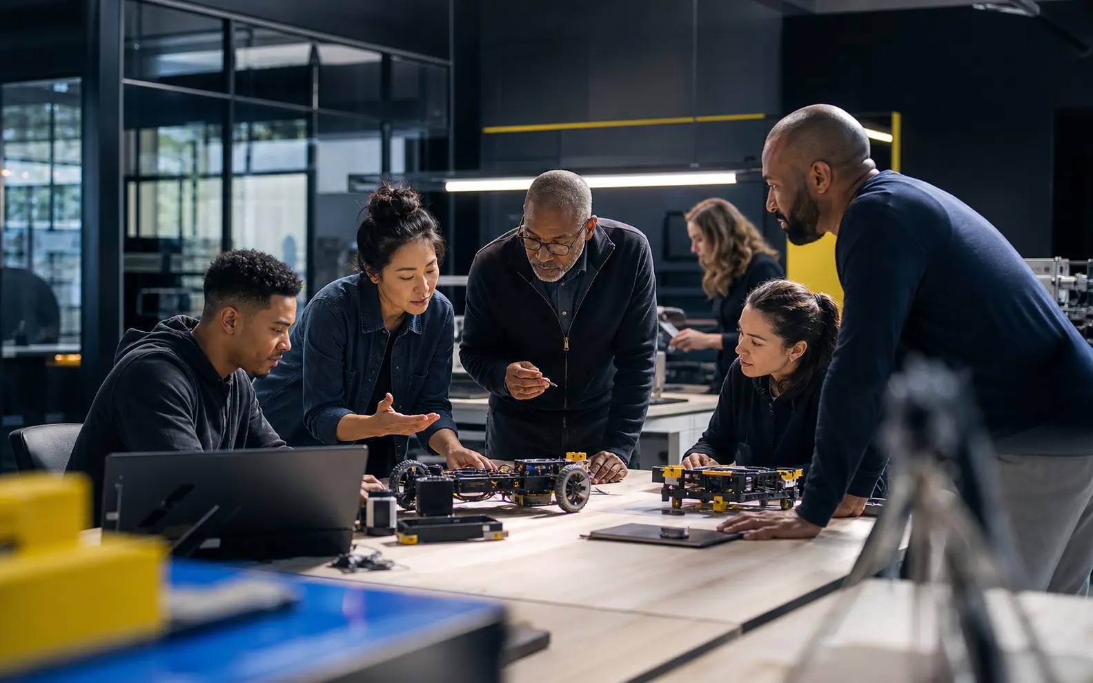 A diverse team collaborates around an advanced prototype in a modern technical workshop.
