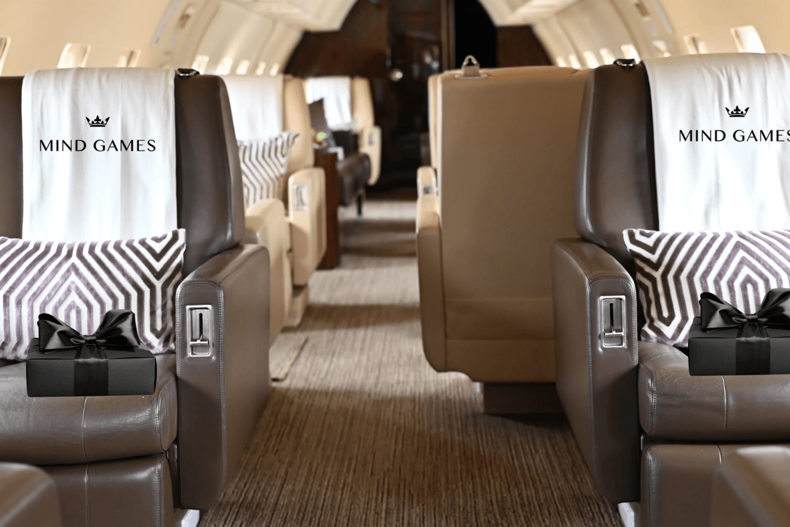 Facing rows of private jet seats, each headrest cover printed with a crown and the words MIND GAMES, with a black gift box on each armrest.