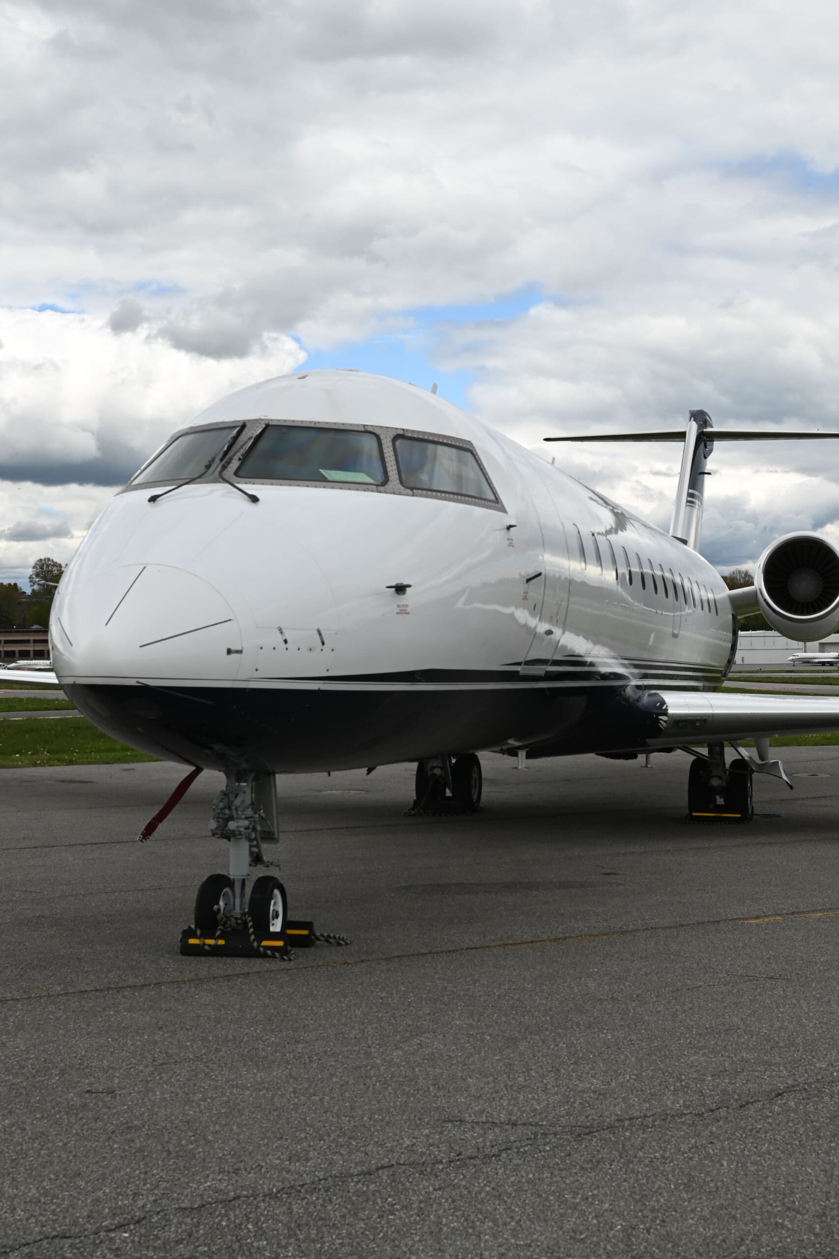 The nose of a white private jet parked on the apron under a clouded sky.