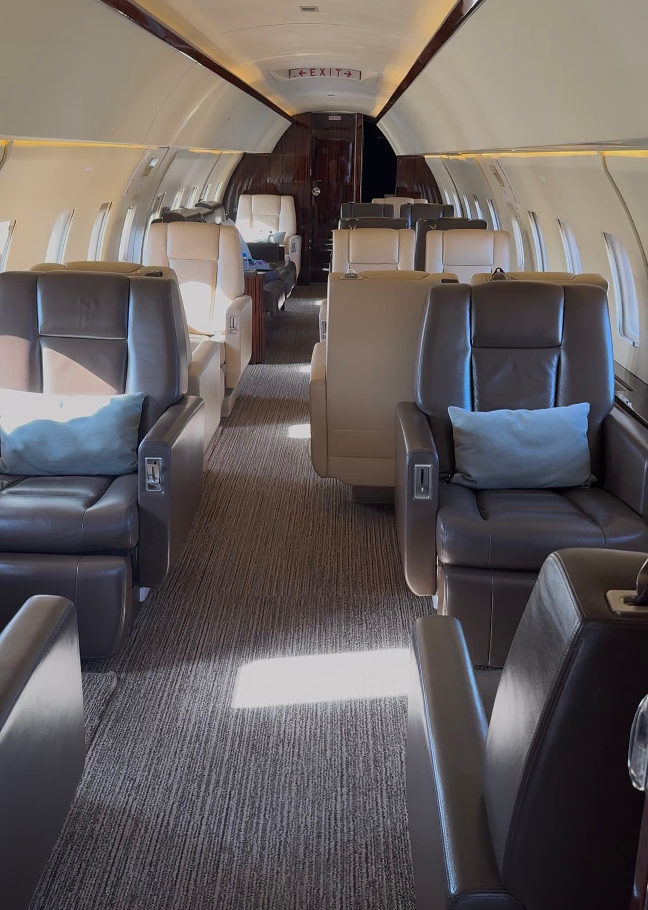 A private jet cabin in daylight, pale blue cushions on the seats and sunlight falling across the aisle.